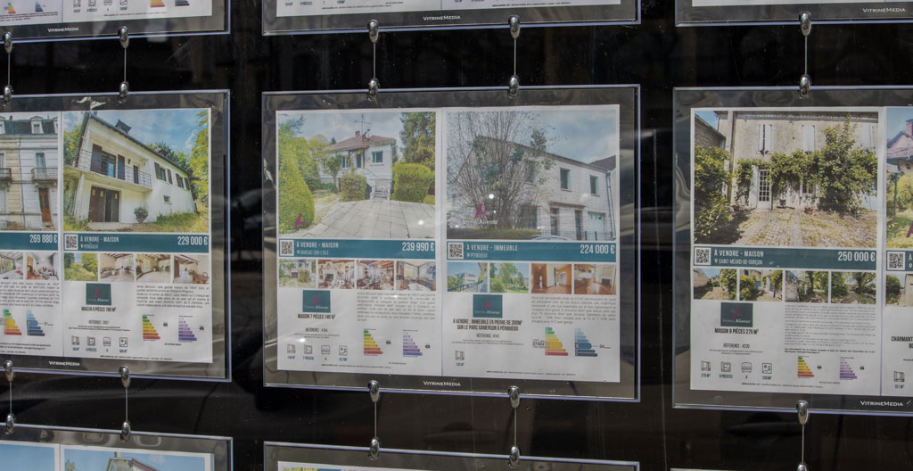 Personne de dos consultant une tablette devant la vitrine d'une agence immobilière moderne à Canet-en-Roussillon